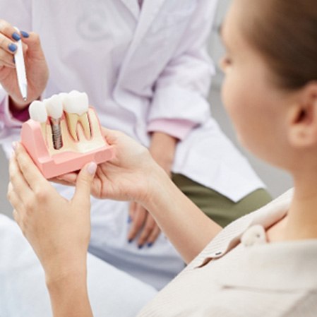 A dentist pointing to a model dental implant