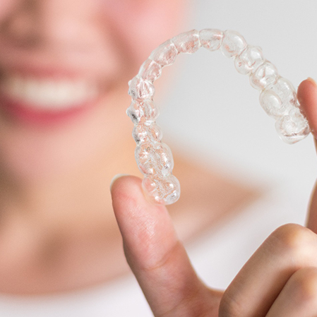 Closeup of smiling patient holding clear aligner
