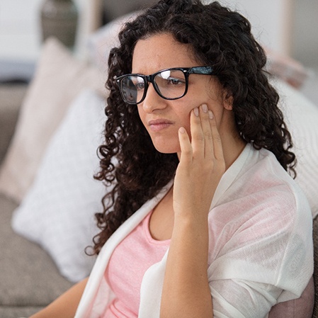 Woman with glasses rubbing jaw and looking concerned