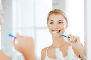 Blonde woman brushing teeth in bathroom mirror